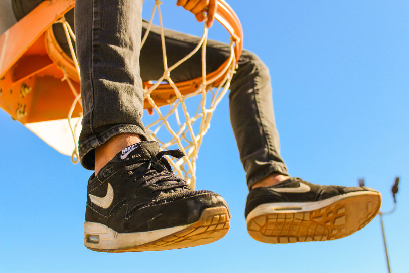 Man wearing Nike sitting on a basketball hoop