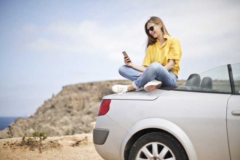 Woman enjoying time with her car while viewing smartphone